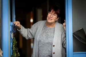 An older woman standing in the doorway of her home. 